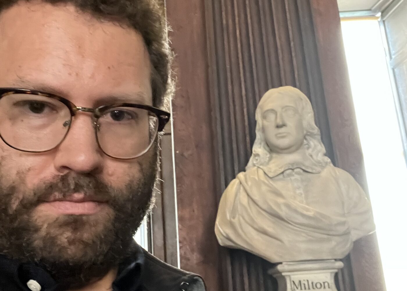 Photograph of a man with a statue behind him.