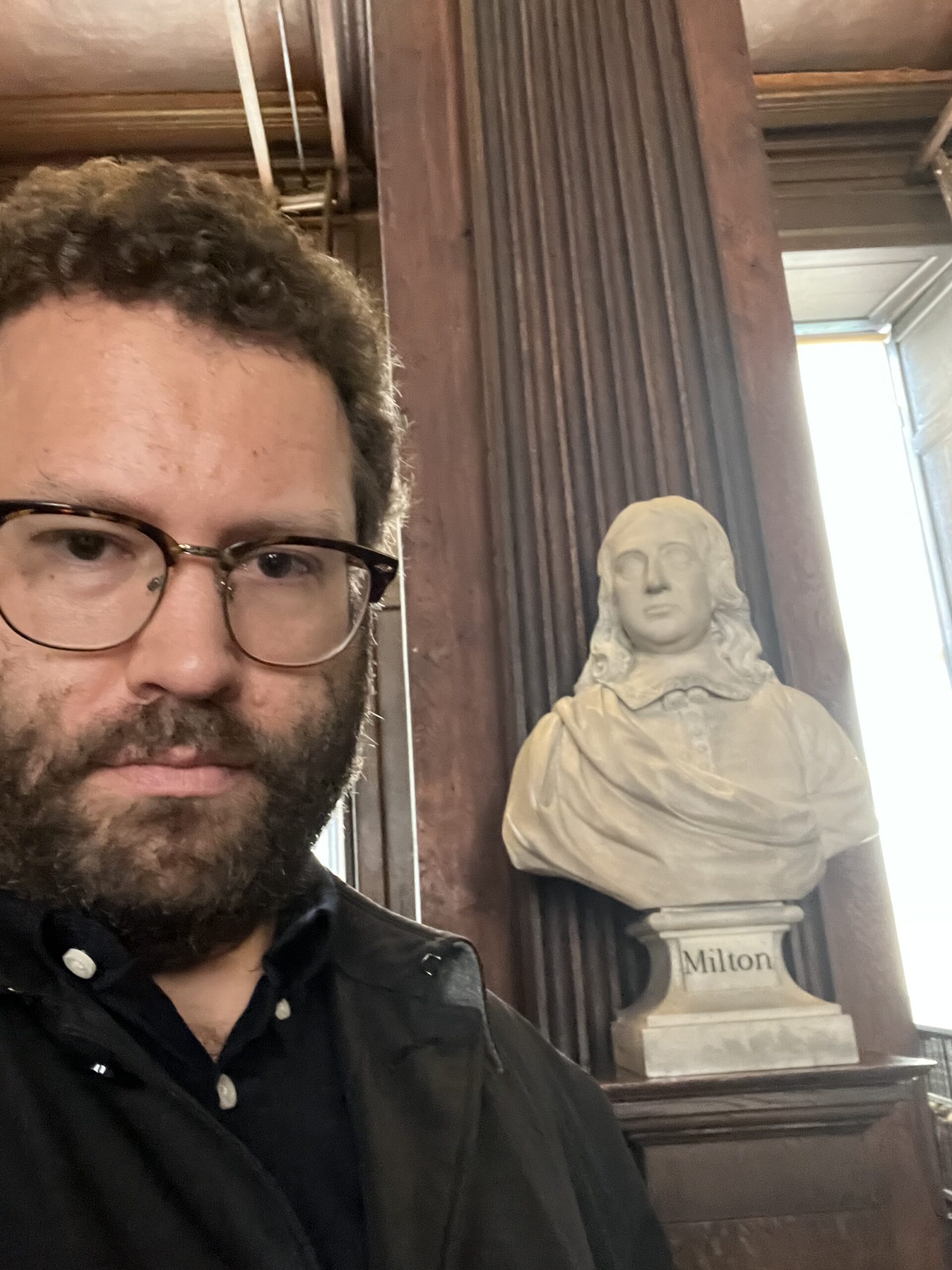 Photograph of a man with a statue behind him.